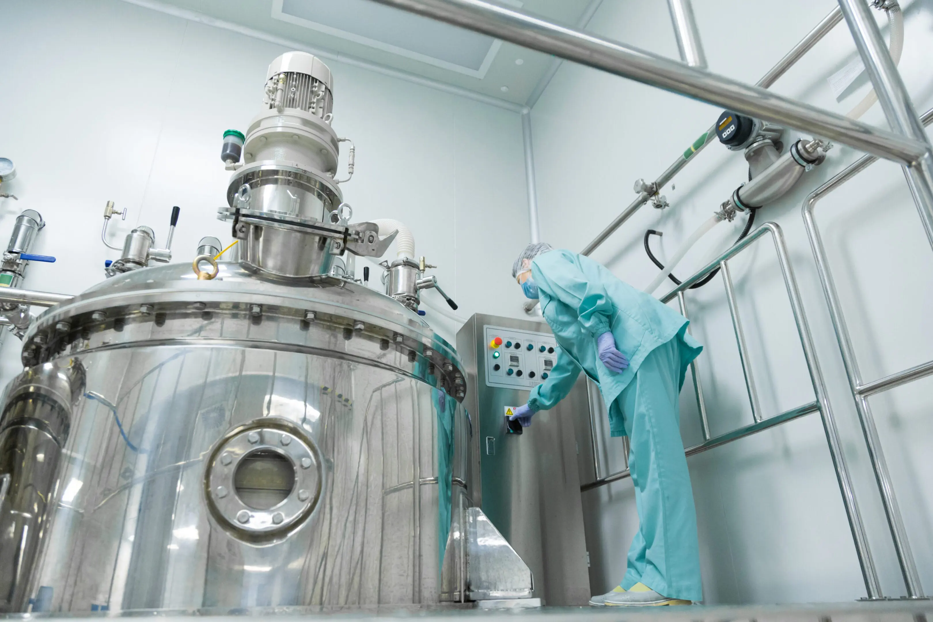 Technician operating a stainless steel industrial bioreactor in a cleanroom.